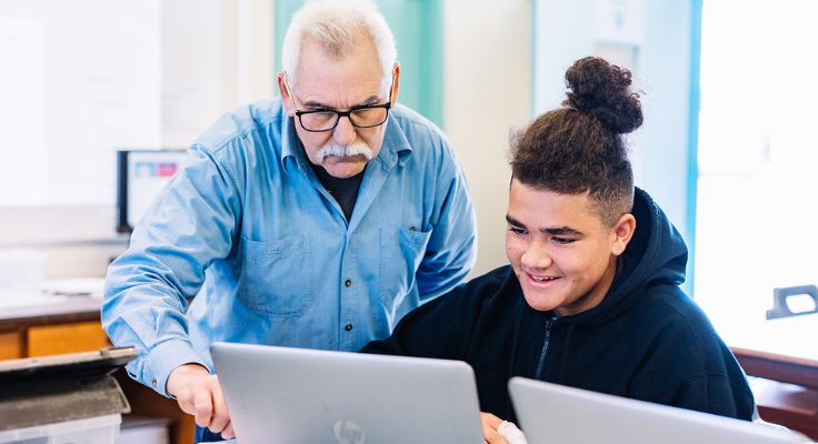 A male teacher and male student working on a laptop computer