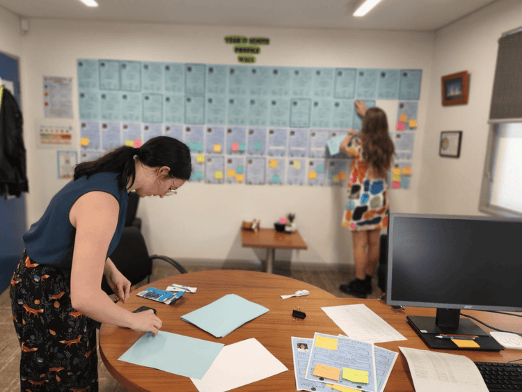 An image of two female teachers placing profile documents on a wall