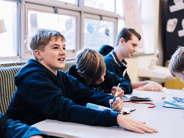 An image of a boy in class smiling with a pen in his hand
