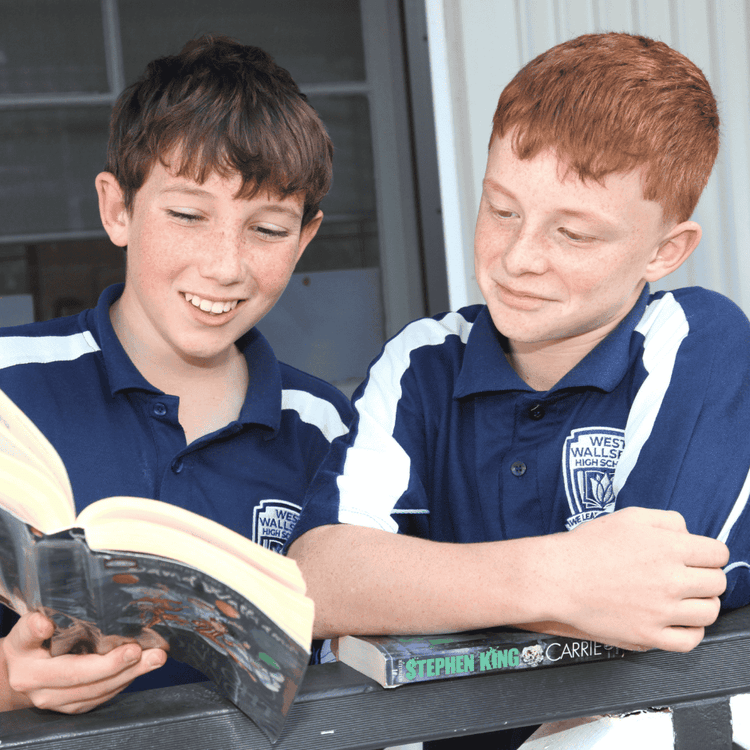 An image of two male students reading a book and smiling